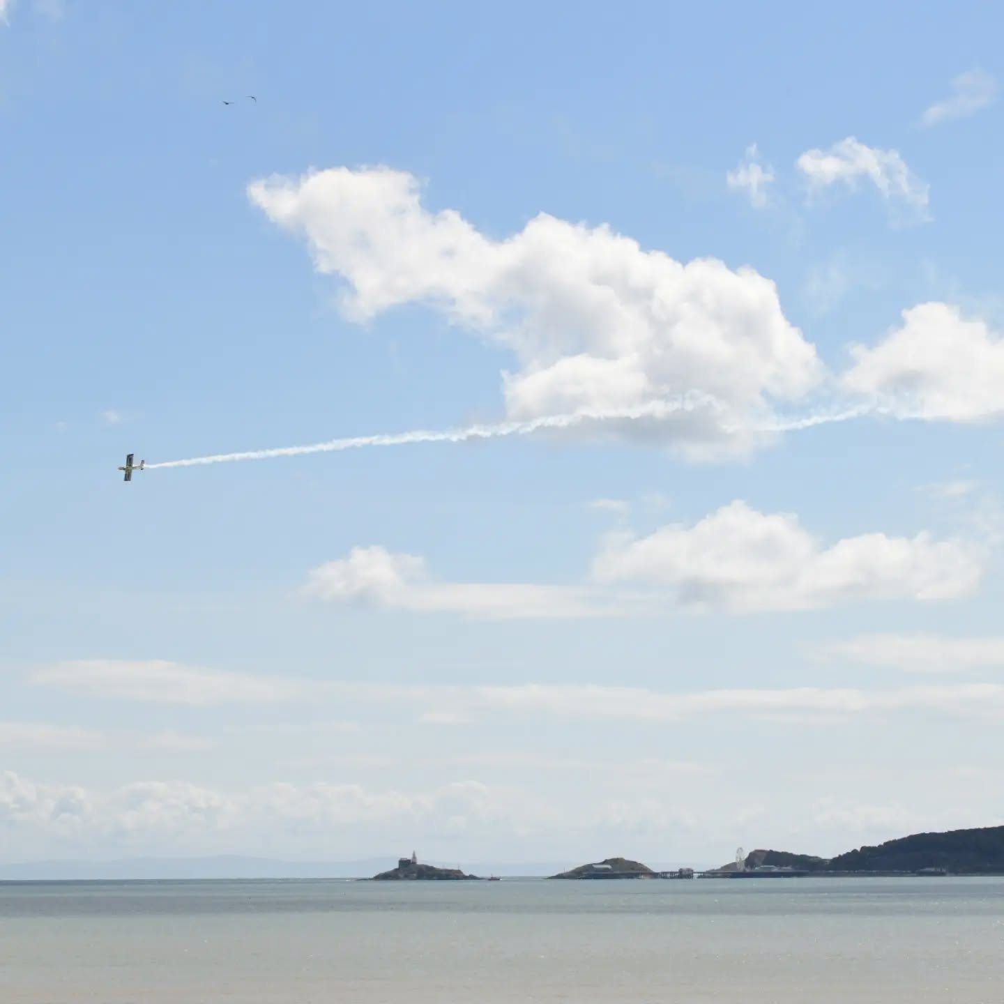 A light aircraft trailing white smoke over Swansea Bay with Mumbles lighthouse and pier in the distance