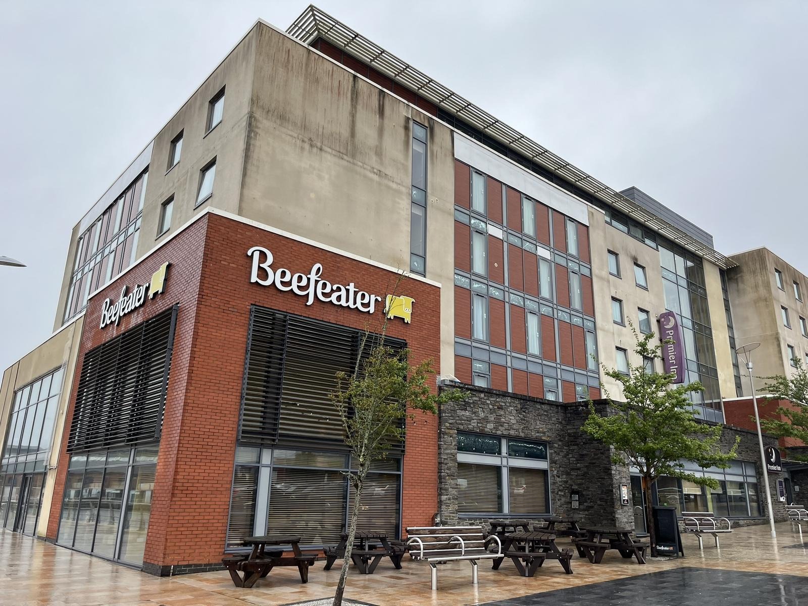 The brick and render exterior of the Waterfront Beefeater on a wet day, with Premier Inn signage on the hotel above and picnic benches outside.