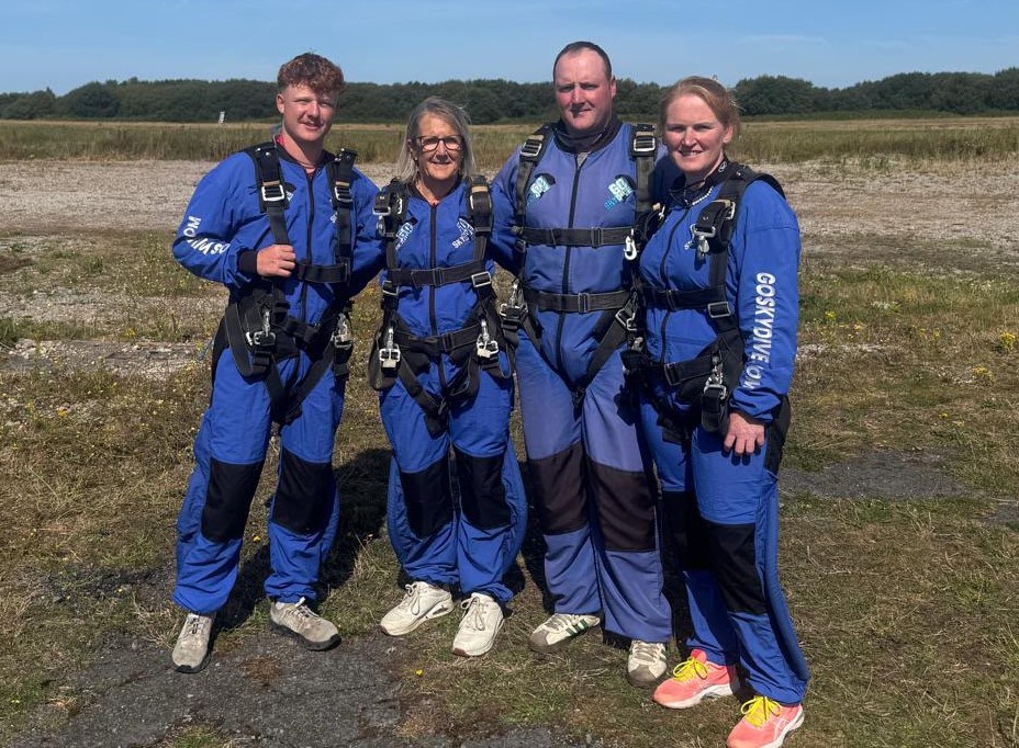 Four skydivers in blue jumpsuits and harnesses standing on the airfield at Swansea Airport