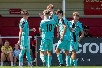 Pure Swansea players in pale blue shirts celebrating a goal in front of the stand at Briton Ferry