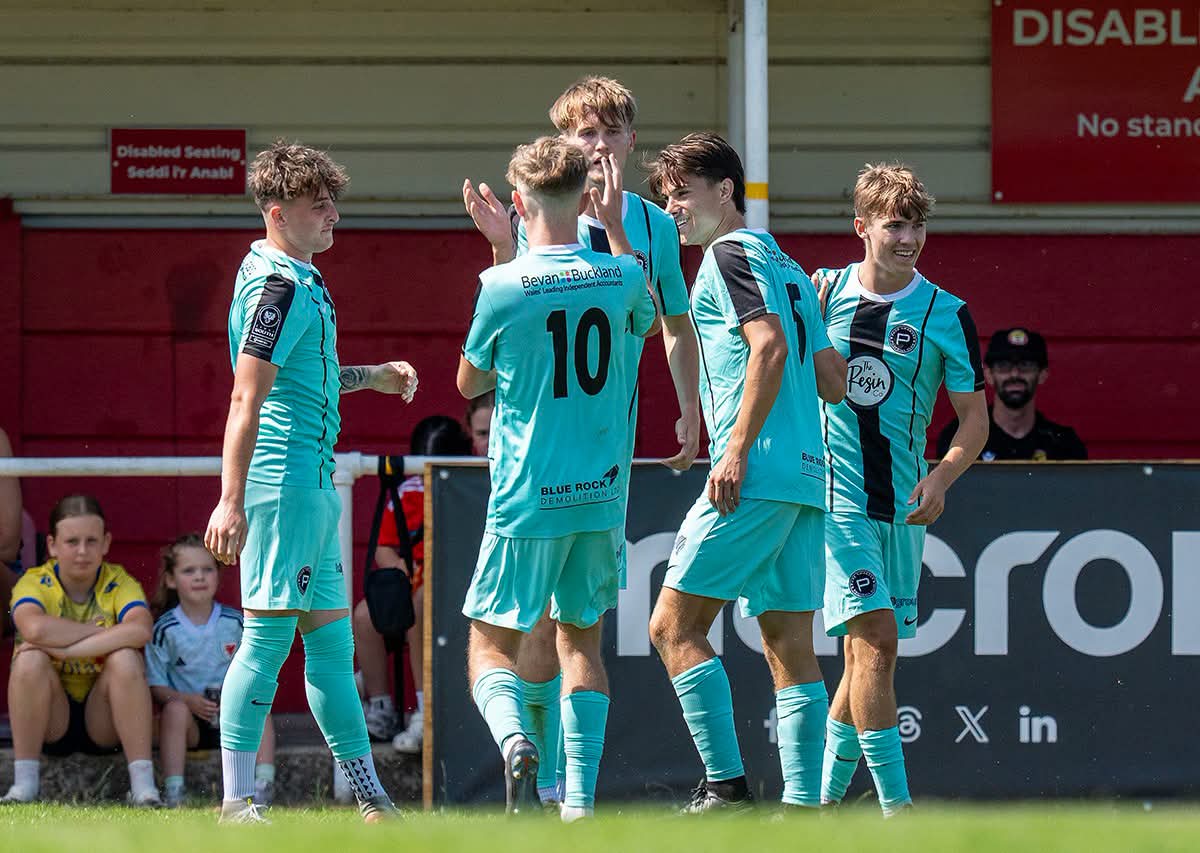 Pure Swansea players in pale blue shirts celebrating a goal in front of the stand at Briton Ferry