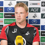 Swansea City defender Stephen Welsh speaking at a press conference in front of a sponsors' backdrop