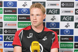 Swansea City defender Stephen Welsh speaking at a press conference in front of a sponsors' backdrop