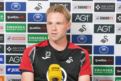 Swansea City defender Stephen Welsh speaking at a press conference in front of a sponsors' backdrop