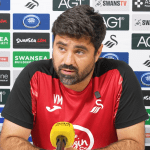 Swansea City head coach Vitor Matos speaking at a press conference in front of a sponsors' backdrop