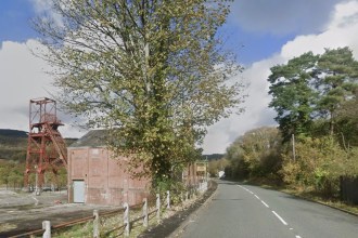 The A4109 road passing the red pithead winding gear and engine house of the former Cefn Coed Colliery in the Dulais Valley