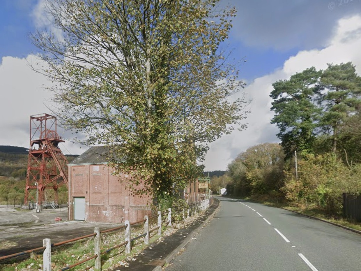 The A4109 road passing the red pithead winding gear and engine house of the former Cefn Coed Colliery in the Dulais Valley