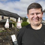 Aaron Jones smiling outside the Penycae Inn, with the stone pub and its hanging sign behind him