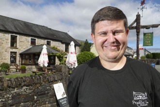 Aaron Jones smiling outside the Penycae Inn, with the stone pub and its hanging sign behind him