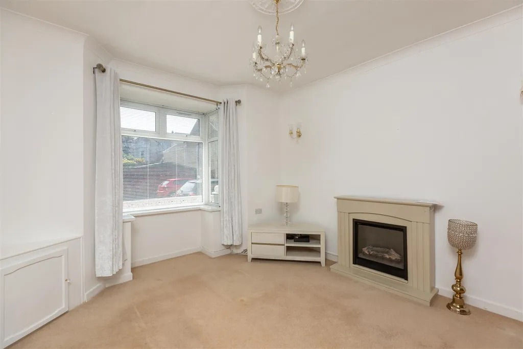 A bay windowed lounge with a fireplace, chandelier and cream carpet