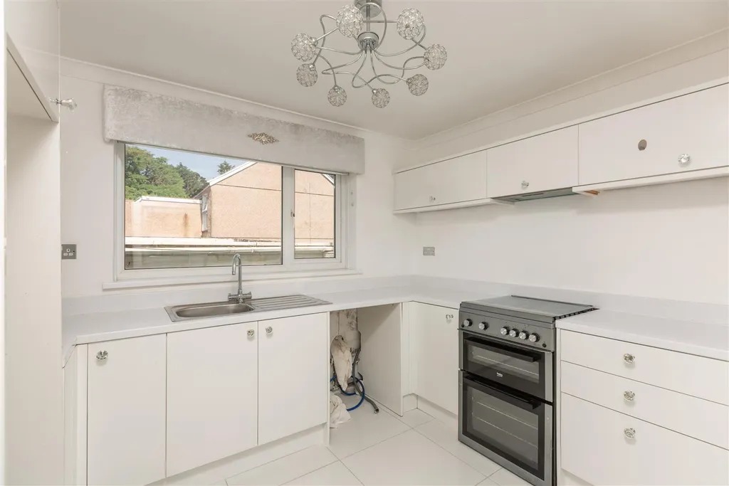A modern white fitted kitchen with an oven, sink and tiled floor