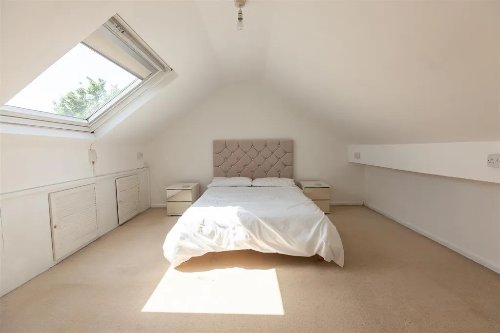 A carpeted loft room with a sloping ceiling, roof window and double bed