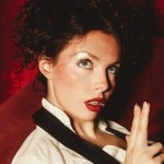 M0Li, a singer with dark curly hair and red lipstick, photographed against red velvet curtains