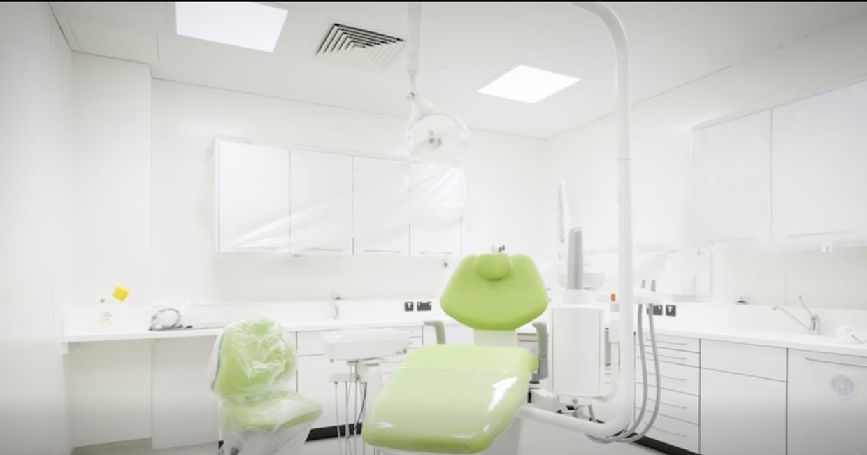 A fitted dental surgery with a green dental chair and white cabinets inside the Atriwm building