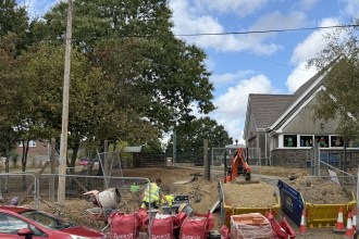 Metal fencing, a cement mixer, bulk bags and a mini digger on bare ground at the entrance to Ysgol Bancyfelin