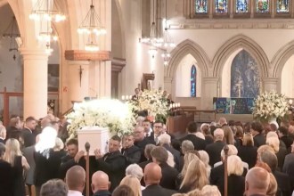 Pallbearers carry a white coffin covered in white flowers up the aisle of Swansea Minster past a packed congregation