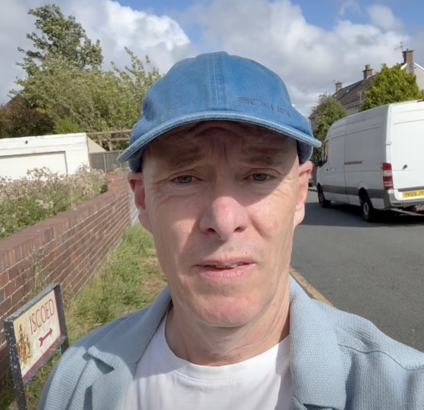 Cllr Martyn Palfreman in a blue cap speaking to camera beside the Iscoed street sign in Llanelli