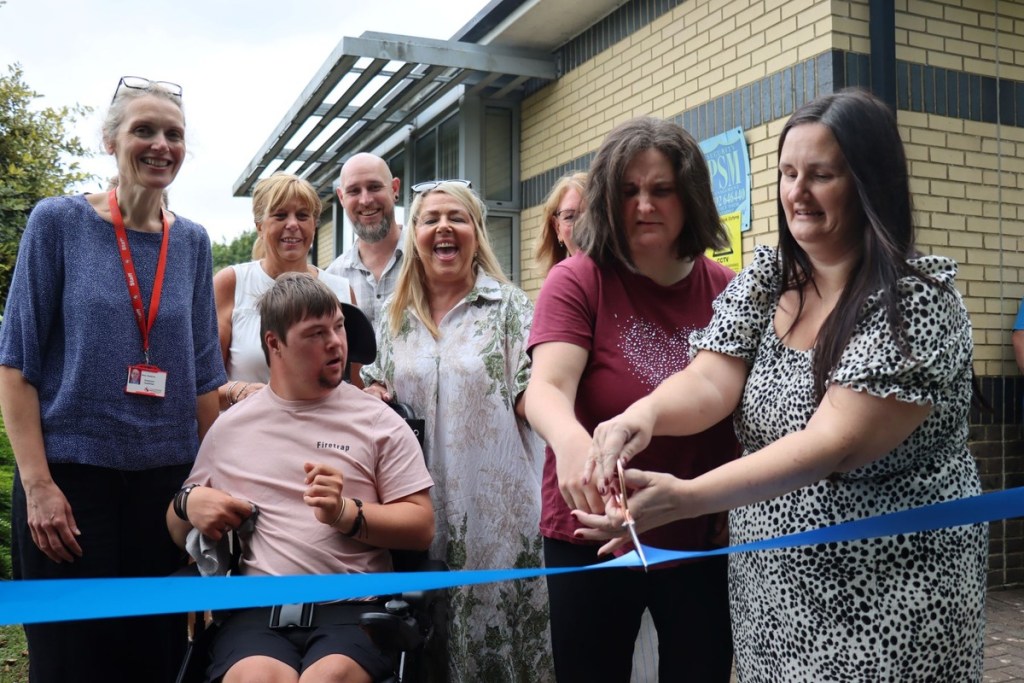 Service users and staff cutting a blue ribbon at the Coed Brân open day in Llansamlet