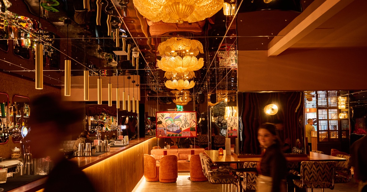The dimly lit interior of a Cosy Club venue with ornate chandeliers, a long bar and patterned seating