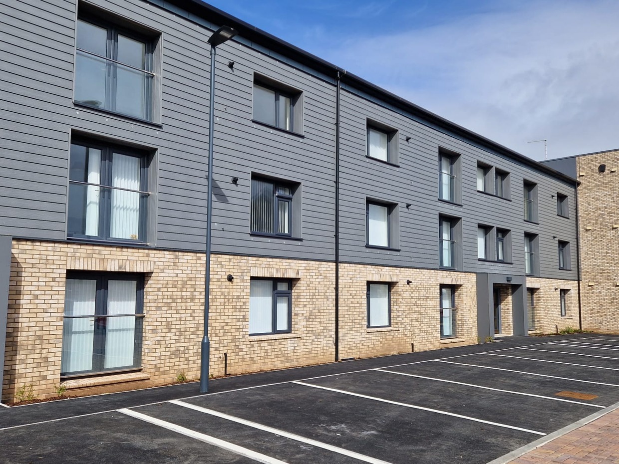 A completed five-storey block at the County Flats in Aberavon, with pale brick, grey cladding and a corner tower, under a blue sky