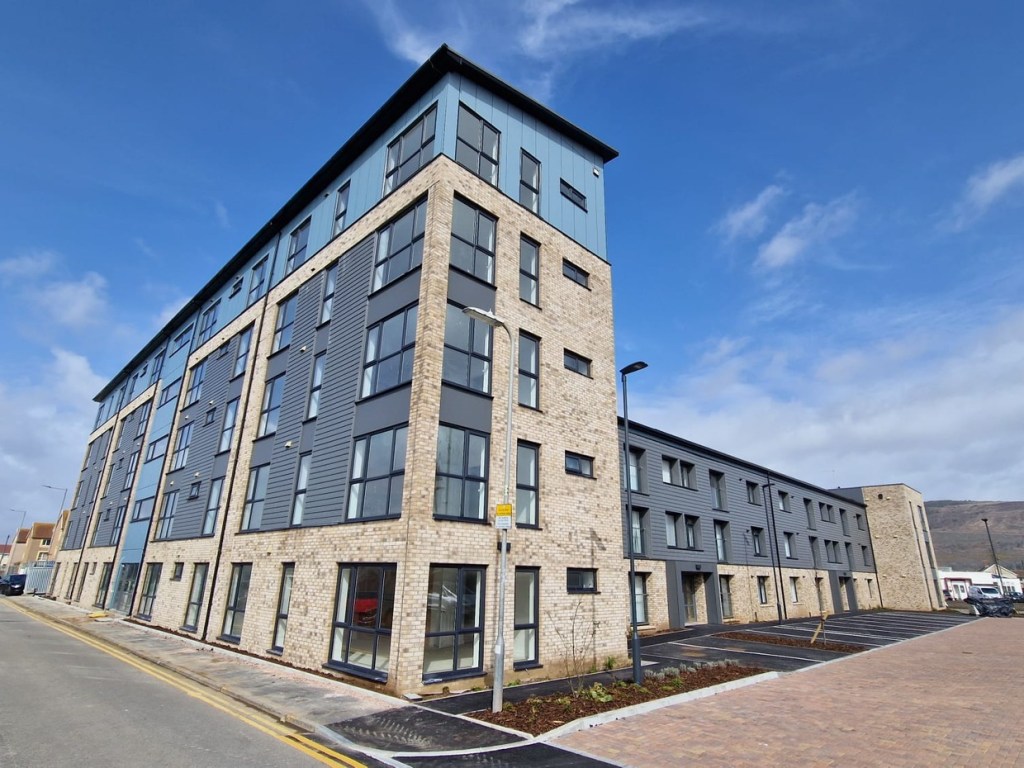Marked parking bays alongside a completed three-storey block at the County Flats in Aberavon, with grey cladding above pale brick