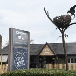 The Crow's Nest pub in Cwmbran, with its grey sign, timber entrance gable and a metal sculpture of a crow on a nest on a tall branch