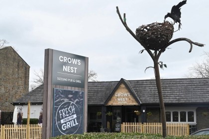 The Crow's Nest pub in Cwmbran, with its grey sign, timber entrance gable and a metal sculpture of a crow on a nest on a tall branch