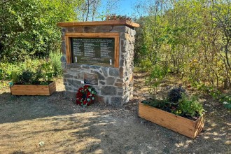 The stone-built Cynheidre Colliery memorial with its black granite plaque, oak frame and a wreath of red roses, flanked by wooden planters