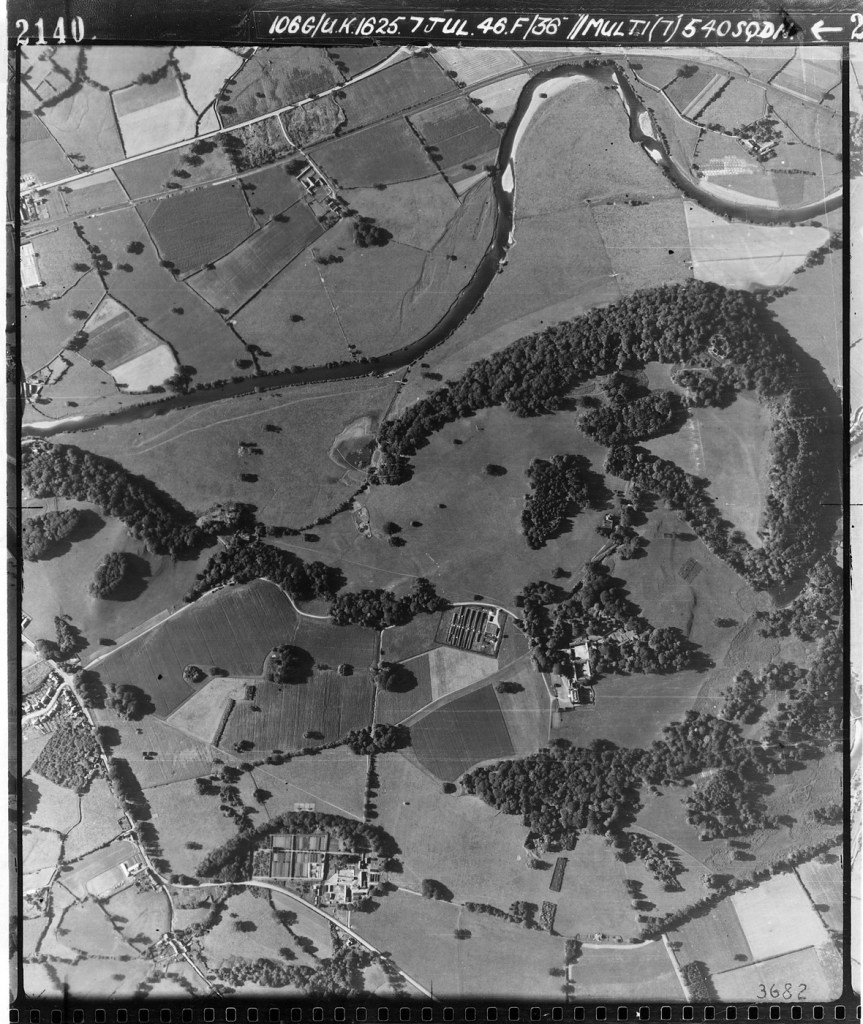 Black and white aerial reconnaissance photograph of parkland, river and fields with rows of huts