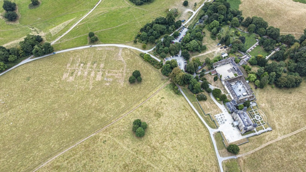 Aerial view of parkland with a large house and pale marks in the grass nearby