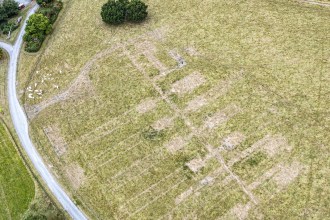 Pale rectangular marks in dry grass showing the foundations of rows of huts