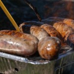 Sausages cooking on a disposable foil barbecue on dry grass