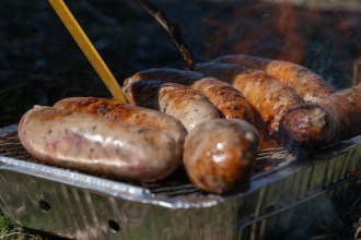 Sausages cooking on a disposable foil barbecue on dry grass