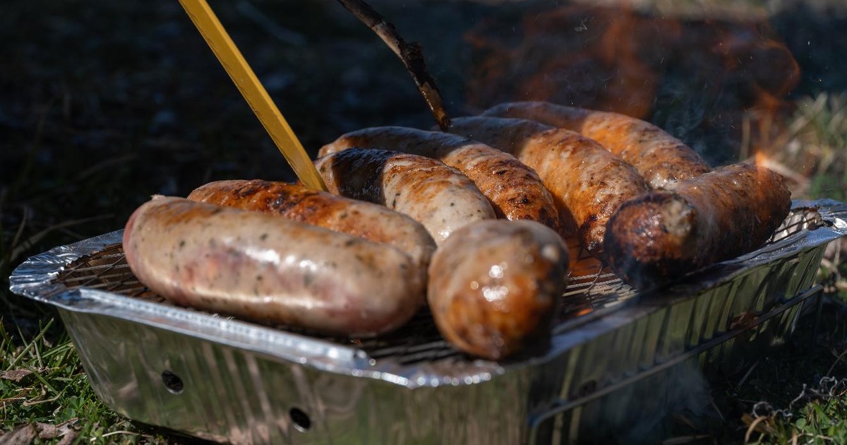 Sausages cooking on a disposable foil barbecue on dry grass