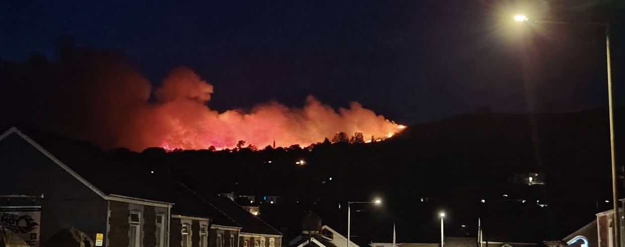 Orange flames and smoke on Drummau Mountain at night above terraced rooftops