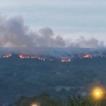 Line of fire and smoke along the ridge of Drummau Mountain at dusk, seen above rooftops