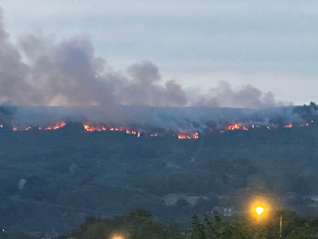 Line of fire and smoke along the ridge of Drummau Mountain at dusk, seen above rooftops