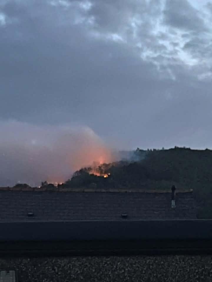 Smoke rising from a hillside above rooftops in morning light
