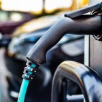 A close-up of an electric vehicle charging cable plugged into a charging point, with a car connected in the background