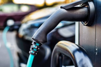 A close-up of an electric vehicle charging cable plugged into a charging point, with a car connected in the background