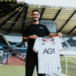 Stephen Eustáquio smiling and holding up a white Swansea City home shirt pitchside at the Swansea.com Stadium