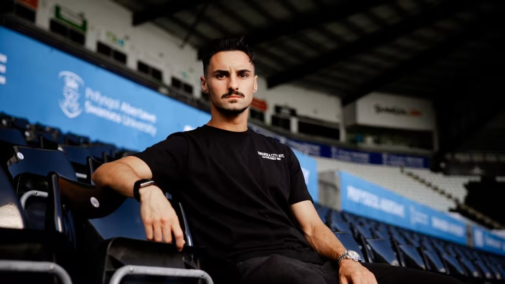 Stephen Eustáquio in a black Swansea City AFC t-shirt sitting in the stands at the Swansea.com Stadium