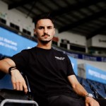 Stephen Eustáquio in a black Swansea City AFC t-shirt sitting in the stands at the Swansea.com Stadium