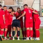 Llanelli Town players in red shirts gather in a huddle on the pitch at Stebonheath before kick-off