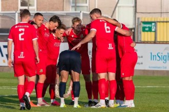 Llanelli Town players in red shirts gather in a huddle on the pitch at Stebonheath before kick-off