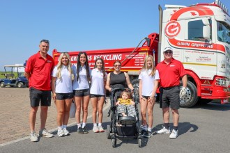 A group including Gavin Griffiths, his family, Liwsi in her buggy with her mother Zoe, and Jake Stephens, standing in front of a red and white Gavin Griffiths tipper lorry at Machynys golf club