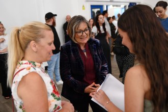Education Minister Anna Brychan smiling as she talks to a student holding a results envelope and her parent in a school hall