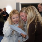 Three teenage girls huddled together reading a GCSE results slip in a school hall, one with a look of surprise