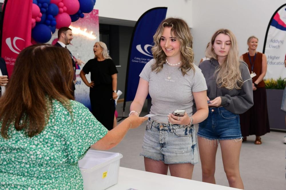 A student smiles as she is handed her results envelope at a collection desk at Gower College Swansea