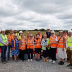 A group of around twenty people in hi-vis vests and hard hats at the Gowerton solar farm site, with panel mounting frames in the fields behind